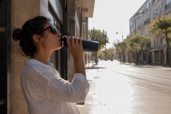 אישה שותה מים מבקבוק ברחוב ישראלי בשמש הכבדה של יום שרבי